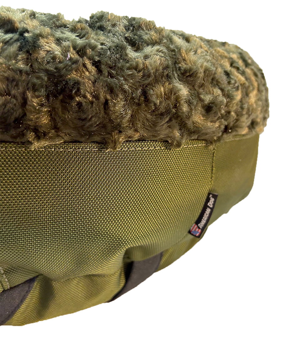 Close-up of a round bolster bed showing olive plush top over green woven fabric base