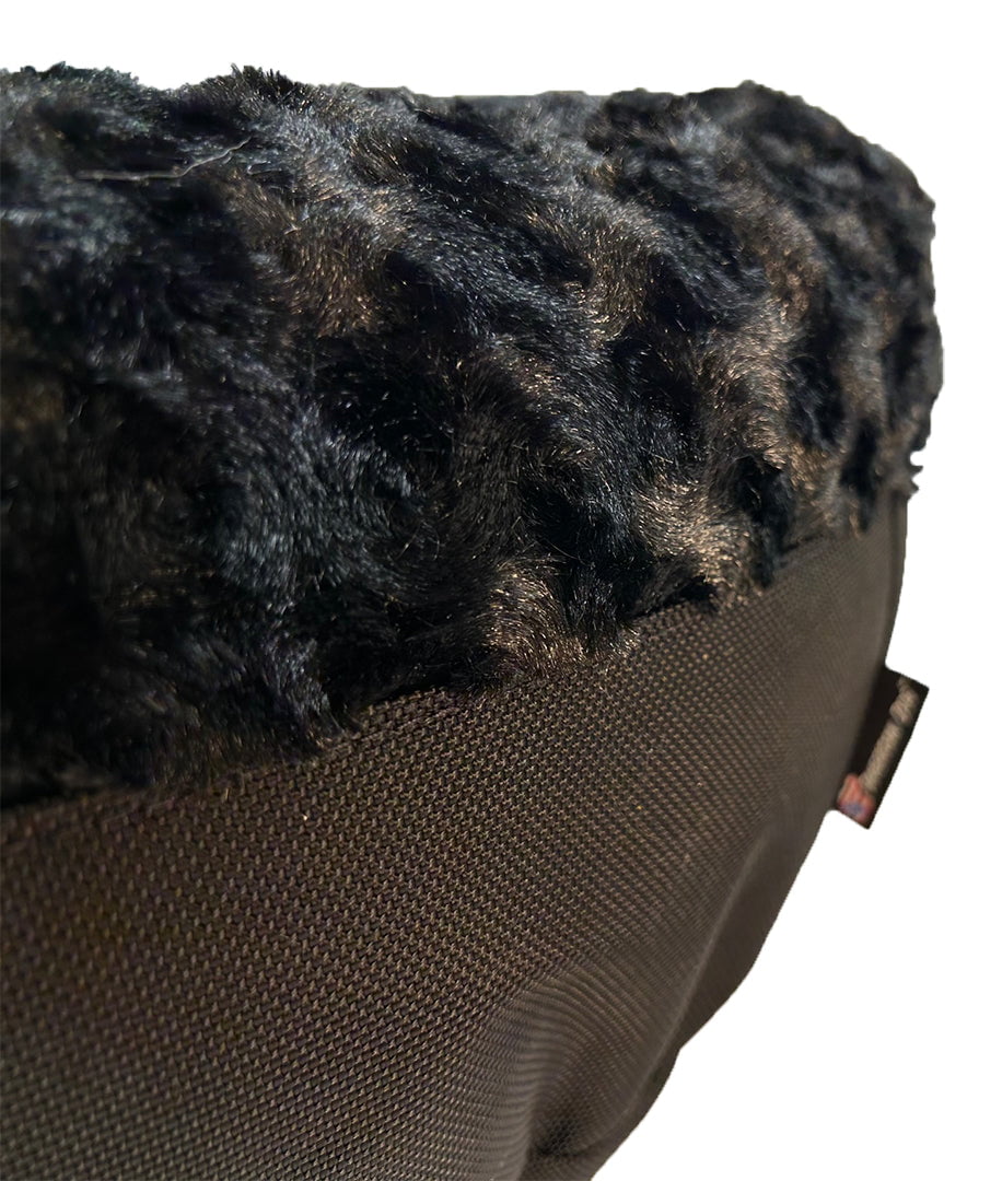 Close-up of a round bolster bed showing black plush fur top over dark woven fabric base